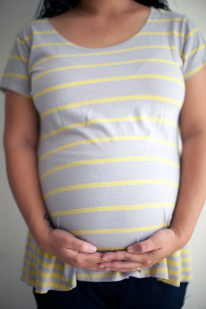 Crop faceless pregnant woman touching belly with both hands